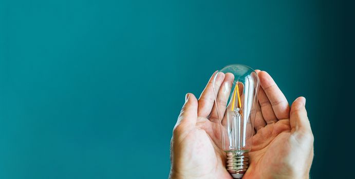 Two hands holding a light bulb on a green background with copy space