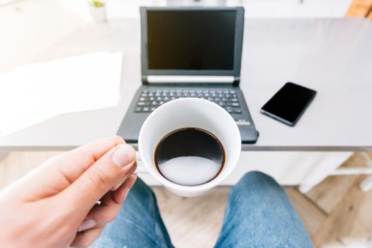 Man teleworking with his tablet, mobile phone and some papers having a coffee at the kitchen table