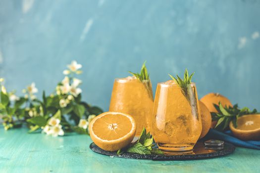 Two glasses of orange ice drink with fresh mint on wooden turquoise table surface. Fresh cocktail drinks with ice fruit and herb decoration. Alcoholic non alcoholic beverage, summer fresh drink