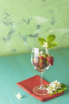 Fresh ripe raw strawberry with green leaves in the wine glass on green surface with red napkin.