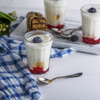 homemade yogurt in transparent glass with syrup and banana on a white wooden background, top view