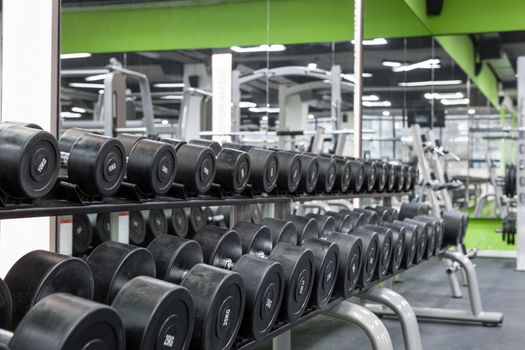 close up black sport dumbbells lie in a row on a stand