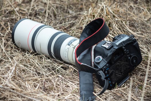 Professional camera lies on dry autumn grass