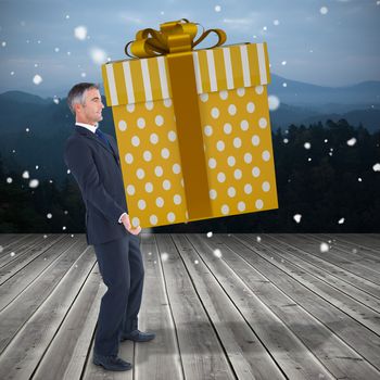 Stylish man with giant gift against wooden planks against mountains