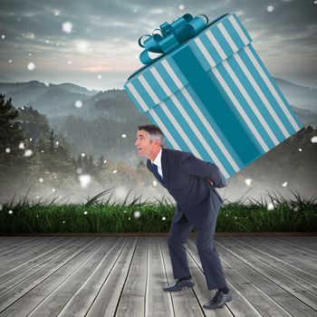 Stylish man with giant gift against mountain range beyond wooden floor