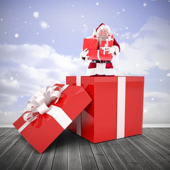 Santa standing in large gift against clouds in a room