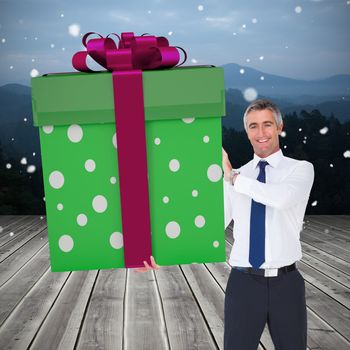 Stylish man with giant gift against wooden planks against mountains