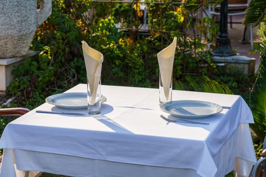 table for two with a white tablecloth in a street restaurant against a background of greenery, selective focus