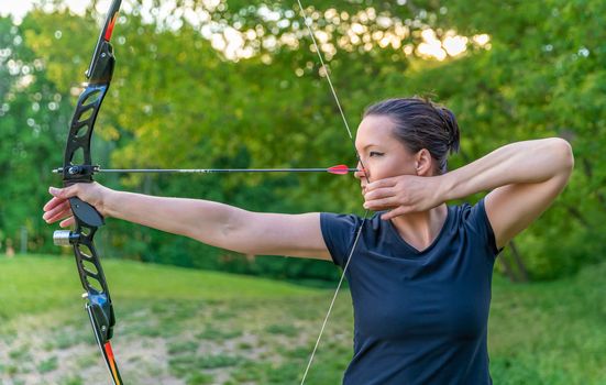 archery, young woman with an arrow in a bow focused on hitting a target.