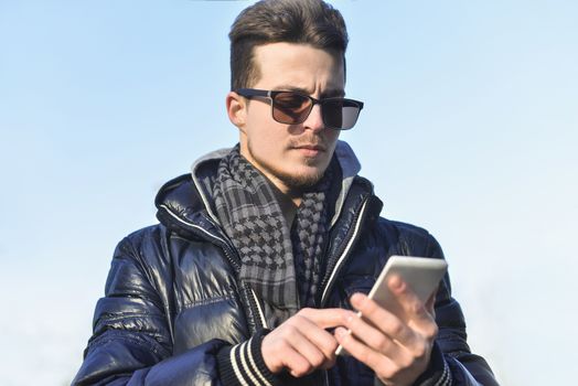 A Guy in a warm jacket with a smartphone in his hands, a sunny day.