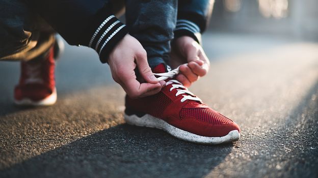 Unrecognizable man stopping lacing shoe outdoors. Athletic shoes concept. Jogging in the park