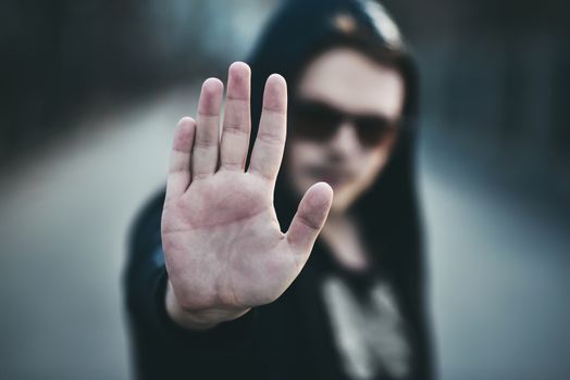 Portrait of fashion man in a black sweater with a hood and sunglasses, hand gestures.