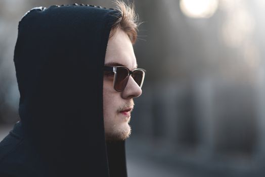 Portrait of fashion man in a black sweater with a hood and sunglasses