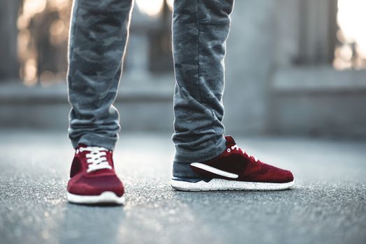 Sports red sneakers close-up on asphalt. Legs and shoes from the lower angle