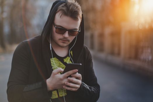 Man in Hood with headphones looking at smartphone.