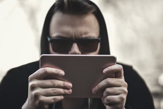 Closeup of a guy in a black hood and a tablet in his hands running on a tablet.