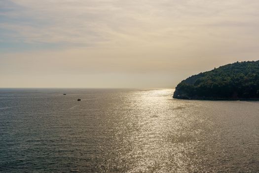 seashore, a hill and ships on the surface of the water at sunset