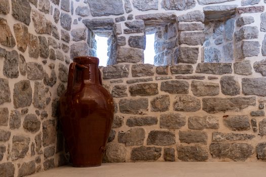 interior in an old Balkan fortress, a large jug against a stone wall with small windows