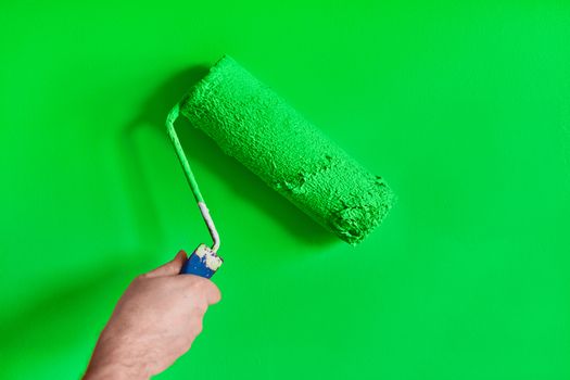 Male hand painting wall with paint roller. Painting apartment, renovating with green color paint