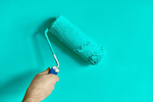 Male hand painting wall with paint roller. Painting apartment, renovating with turquoise color paint