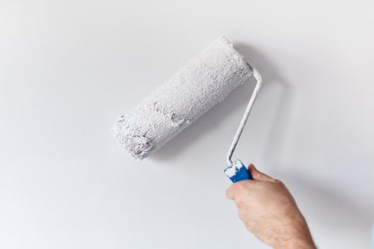 Male hand painting wall with paint roller. Painting apartment, renovating with white color paint