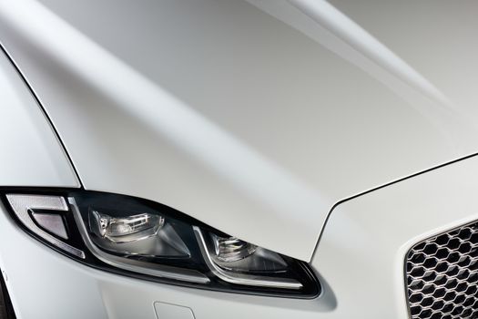 The headlight and bonnet of a white car. A modern and luxurious car.