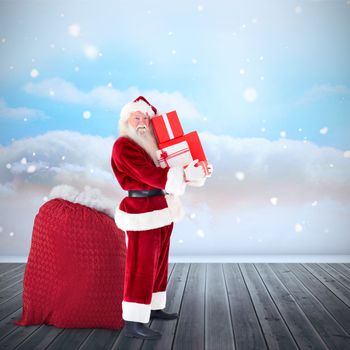 Santa claus carrying pile of gifts against clouds in a room