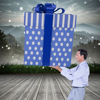 Stylish man with giant gift against mountain range beyond wooden floor