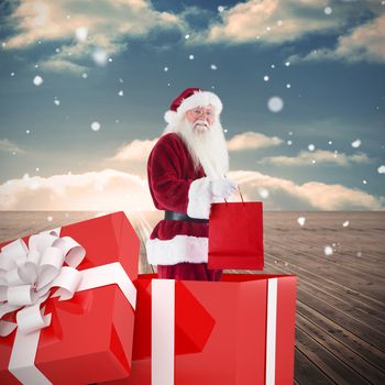Santa standing in large gift against wooden planks leading to blue sky