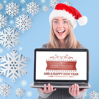 Festive blonde holding a laptop against snow flake frame design on blue