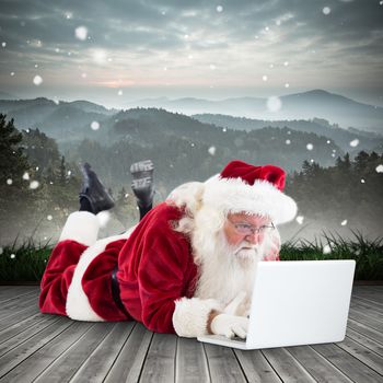 Santa lies in front of his laptop against mountain range beyond wooden floor