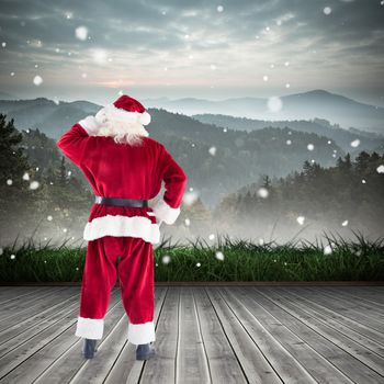 Santa scratching his head against mountain range beyond wooden floor