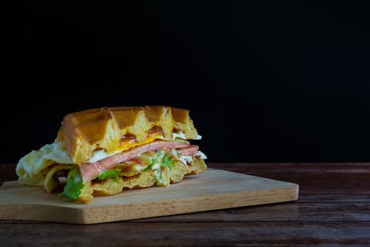 Waffle sandwich with fresh lettuce fried egg and ham with tomato sauce on chopping board and black background. Copy space for your text.