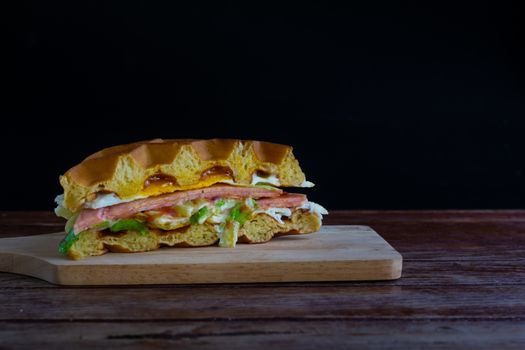 Waffle sandwich with fresh lettuce fried egg and ham with tomato sauce on chopping board and black background. Copy space for your text.