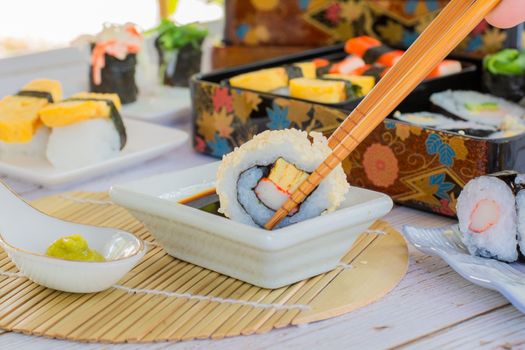 Eatting tamagoyaki maki and white sesame seeds with wooden chopsticks and soy sauce in white bowl. Delicious japanese food.