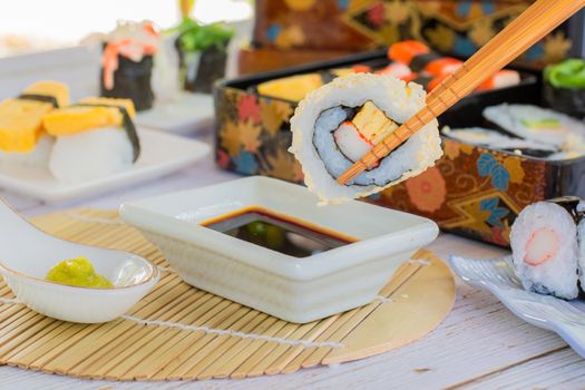 Eatting tamagoyaki maki and white sesame seeds with wooden chopsticks and soy sauce in white bowl. Delicious japanese food.