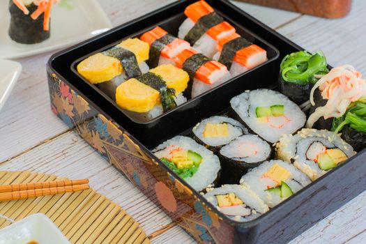 Set of variety sushi, Tamagoyaki, crabsticks sushi and maki in bento box served with soy sauce and wasabi. Delicious japanese food.