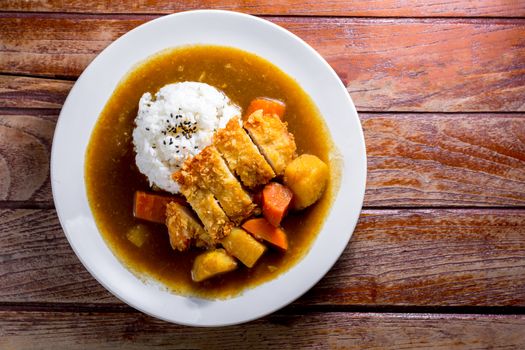 Japanese curry with rice, black sesame, carrot, potato and deep fries chicken in white dish on wooden table.