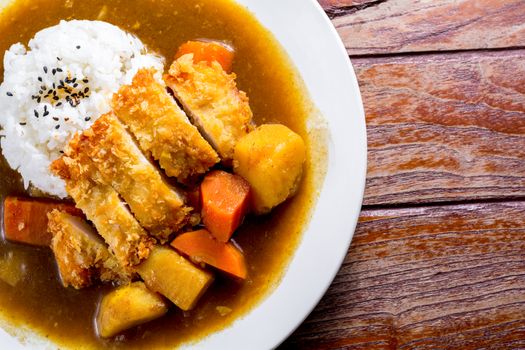 Japanese curry with rice, black sesame, carrot, potato and deep fries chicken in white dish on wooden table.