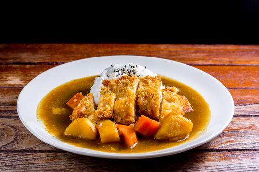 Japanese curry with rice, black sesame, carrot, potato and deep fries chicken in white dish on wooden table.