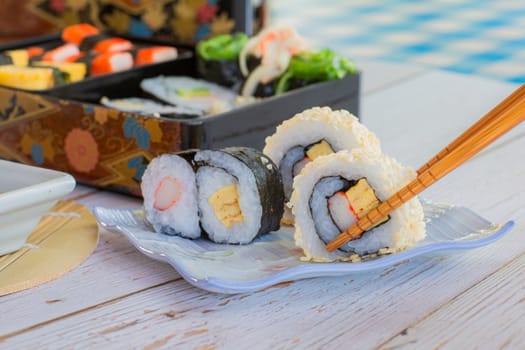 Eatting tamagoyaki maki and white sesame seeds with wooden chopsticks and soy sauce in white bowl. Delicious japanese food.