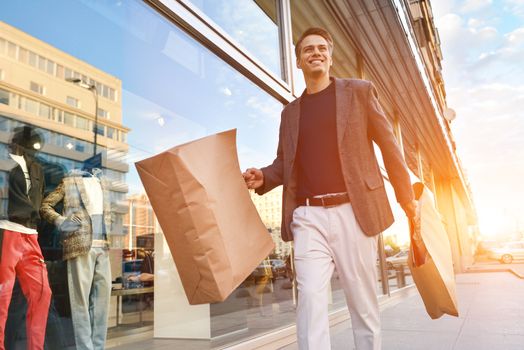 Serious cool guy with shopping paper bags walking at street.