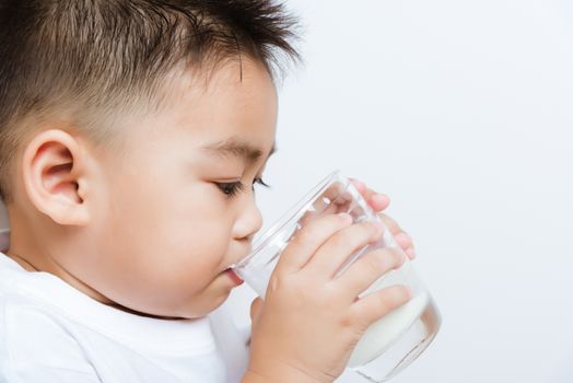 Close up of happy Asian little cute child boy hand holding milk glass he drinking white milk during sitting on the sofa at home after lunch. Daily life health care Medicine food