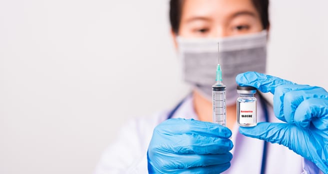Asian female woman doctor or nurse in uniform and gloves wearing face mask protective in lab hold needle syringe drug and medicine vial vaccine bottle and on bottle has "COVID-19 VACCINE" text label