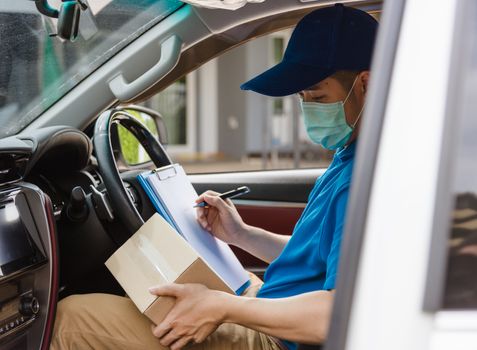 Asian delivery courier young man driver inside the van car with parcel post boxes checking amount he protective face mask, under curfew quarantine pandemic coronavirus COVID-19