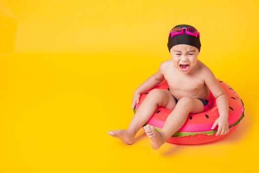 Summer vacation concept, Portrait Asian happy cute little child boy wear goggles, swimsuit hold beach watermelon inflatable ring, Kid have fun sit in inflatable, studio shot isolated yellow background