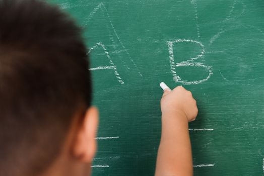 Back to School. Happy Asian funny back of cute little child boy kindergarten preschool in student uniform writing ABC with white chalk on green school blackboard, First time to school education