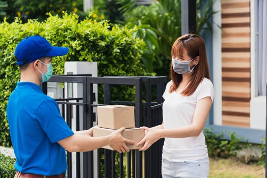 Asian young delivery man courier shopping online give package post box he protective face mask service woman customer receiving box at front home, under curfew quarantine pandemic coronavirus COVID-19