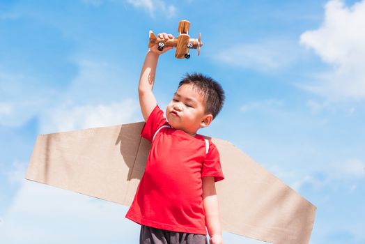 Happy Asian funny child or kid little boy smile wear pilot hat play and goggles with toy cardboard airplane wing flying hold plane toy outdoor against summer blue sky cloud background, Startup freedom