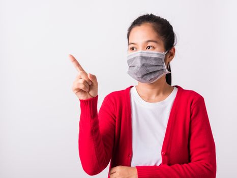 Asian adult woman wearing red shirt and face mask protective against coronavirus or COVID-19 virus or filter dust, air pollution her point finger to side space, studio shot isolated white background